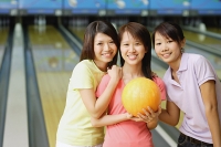 Three women at bowling alley, smiling at camera - Asia Images Group