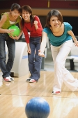 Woman bowling, friends behind her, watching - Asia Images Group