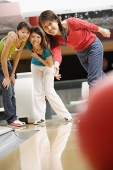 Three women at a bowling alley, bowling ball in the foreground - Asia Images Group
