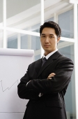 Businessman standing next to flipchart, arms crossed - Asia Images Group