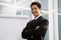 Businessman standing next to flipchart, smiling, arms crossed - Asia Images Group