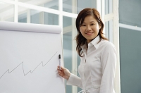 Businesswoman looking at camera, standing next to flipchart - Asia Images Group