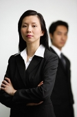 Businesswoman with arms crossed, man in the  background - Asia Images Group