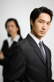 Businessman looking at camera, woman in the  background - Asia Images Group