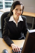 Businesswoman sitting at desk, using computer, smiling at camera - Asia Images Group