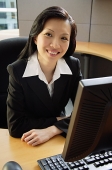 Businesswoman sitting at desk, smiling at camera - Asia Images Group