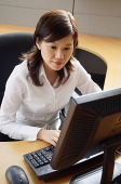 Businesswoman sitting in office cubicle, looking at computer - Asia Images Group