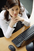 Businesswoman sitting in office cubicle, hands on chin, looking up at camera - Asia Images Group