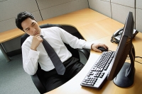 Businessman sitting at desk, looking at computer - Asia Images Group
