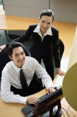 Businessman and woman in office cubicle, looking up at camera, smiling - Asia Images Group