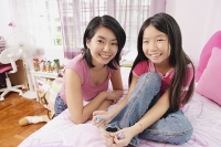 Mother and daughter smiling at camera, daughter painting toenails - Asia Images Group