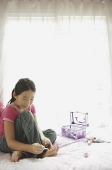 Girl sitting on bed, painting toenails - Asia Images Group