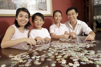 Family of four in living room working on jigsaw puzzle - Asia Images Group