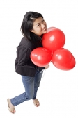 Woman holding red balloons, looking up, smiling - Asia Images Group