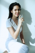 Young woman sitting, holding glass, looking at camera - Asia Images Group