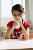 Girl sitting at table, drinking glass of milk - Asia Images Group