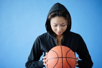 Woman wearing hooded shirt, holding basketball - Asia Images Group