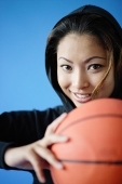 Woman wearing hooded shirt, holding basketball, smiling - Asia Images Group