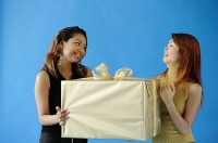 Two woman carrying big gift box, smiling at each other - Asia Images Group