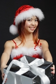 Woman in Santa hat and red dress, holding silver gift box - Asia Images Group