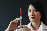 Female doctor looking at syringe, serious expression - Asia Images Group