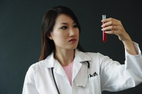 Doctor looking at test tube, serious expression - Asia Images Group