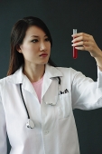 Female doctor looking at test tube, serious expression - Asia Images Group