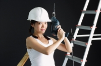 Young woman wearing hard hat, holding drill - Asia Images Group