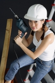 Young woman in hard hat, holding drill, sitting on ladder - Asia Images Group