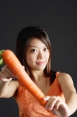 Young woman holding carrot, looking at camera - Asia Images Group