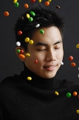 Young man dressed in black, multi coloured candy in the air around him - Asia Images Group