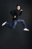 Young man dressed in black jumping and smiling at camera - Asia Images Group