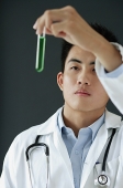 Doctor looking at test tube filled with green liquid - Asia Images Group