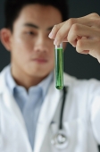 Doctor looking at test tube filled with green liquid - Asia Images Group