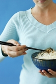 Woman holding bowl of rice in one hand and chopsticks in the other - Asia Images Group