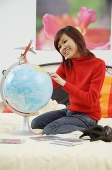 Girl on bed, holding toy airplane and looking at globe - Asia Images Group