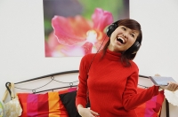 Girl in bedroom, listening to headphone, smiling - Asia Images Group