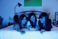 Three girls in bedroom, lying on bed, smiling at camera - Asia Images Group