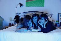 Three girls in bedroom, lying on bed, watching TV - Asia Images Group