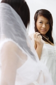 Young woman in white dress and veil, looking at mirror - Asia Images Group