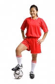 Young woman in soccer uniform, standing with foot on ball and hands on hips - Asia Images Group