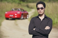 Man wearing sunglasses, arms crossed, facing camera, red sports car in the background - Asia Images Group