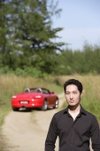 Man looking at camera, red sports car in the background - Asia Images Group