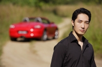 Man looking at camera, red sports car in the background, portrait - Asia Images Group