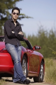 Man wearing sunglasses, arms crossed, leaning on red sports car - Asia Images Group