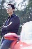 Man wearing sunglasses, leaning on red sports car, looking away - Asia Images Group