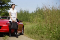 Woman standing next to red sports car, carrying bag - Asia Images Group
