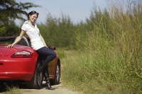 Woman leaning on red sports car, smiling at camera - Asia Images Group