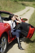 Woman sitting in red sports car, shielding eyes - Asia Images Group