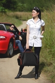 Woman in foreground carrying bag, man sitting in red sports car in the background - Asia Images Group
